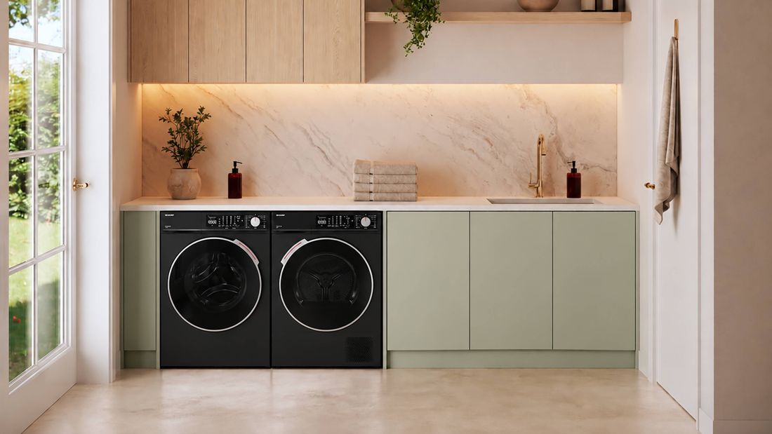 Modern laundry featuring black front-loading washing machine and dryer, sage green cabinetry, marble-look splashback and timber overhead cupboards.