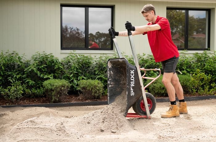 A person in a red shirt is adding crusher dust  on top of the crushed rock to prepare the top layer for synthetic turf installation.