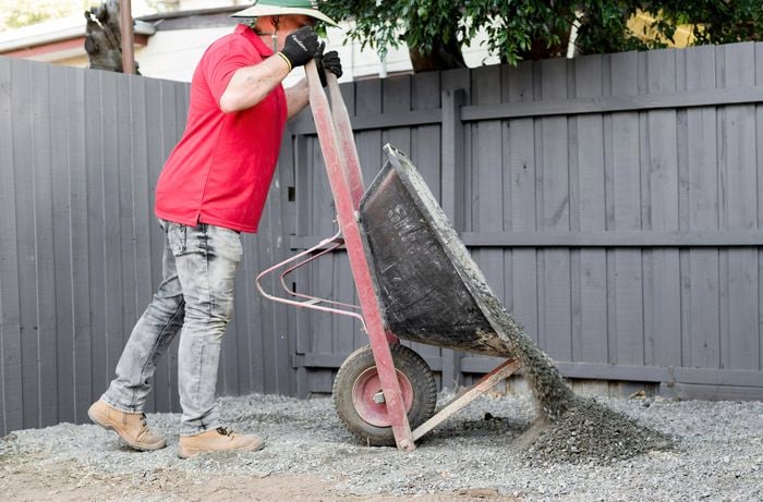 Person in a backyard emptying gravel out of a wheelbarrow.