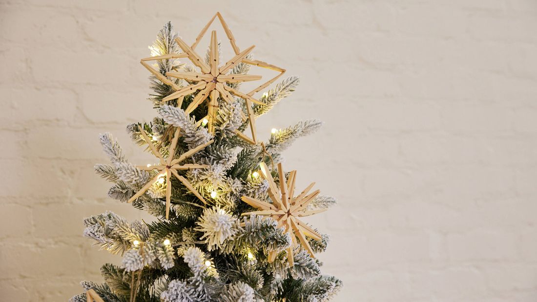 Handmade star ornaments crafted from wooden pegs hanging on a Christmas tree with fairy lights.