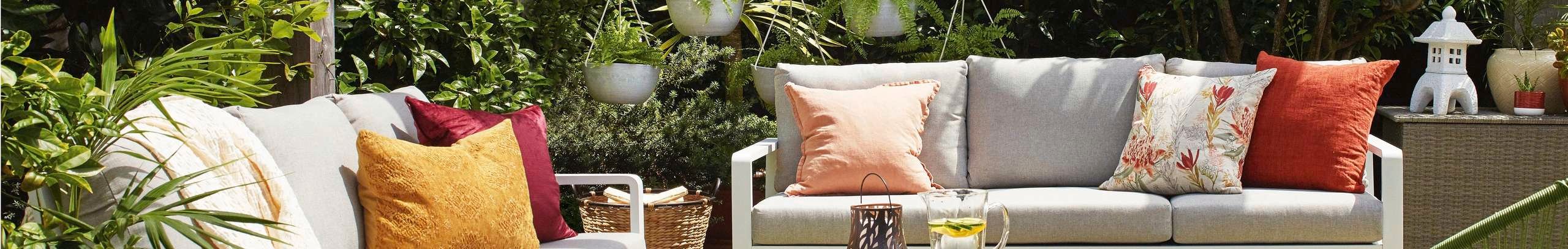 Paved courtyard surrounded by plants and trees, with two outdoor sofas, a table and a lounge chair