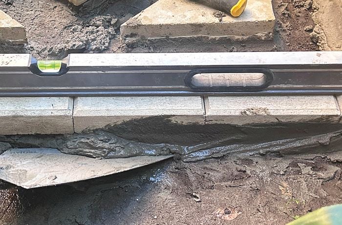 An image of using a shovel to haunch the edges of a stepping stone pathway