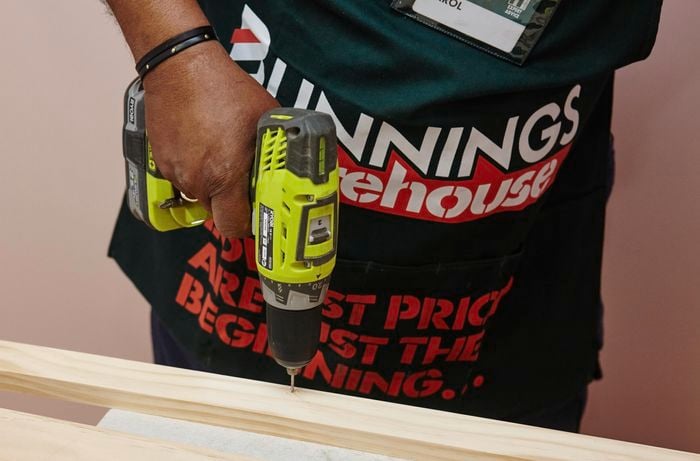 A person drilling a hole in a length of pine timber