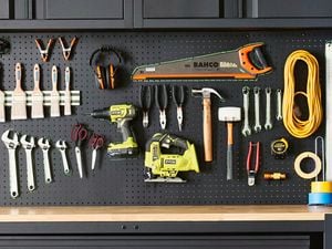 A black wall-mounted pegboard with neatly hanging tools, paintbrushes, cables and headphones.