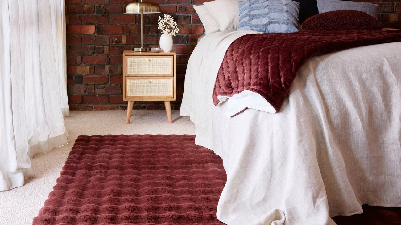 Featured red brick wall in bedroom with bed, timber side table and  lush red rug