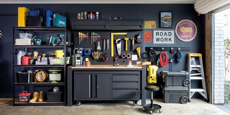 A garage with workbenches, storage cabinets, tools and old signs hanging on the walls.