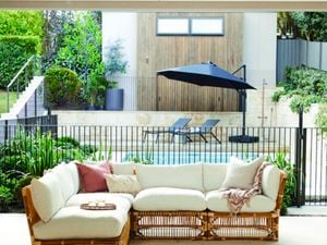 Outdoor lounge in the foreground with a pool, umbrella and sunlounges in the background.