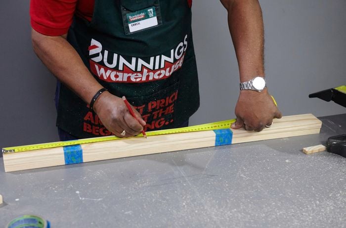A person measuring lengths of pine timber taped together