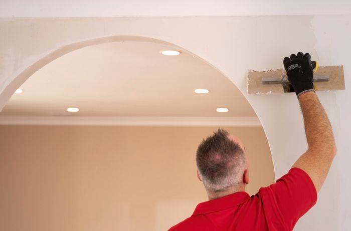 A Bunnings Team Member is smoothing plaster above an archway to blend it into the surrounding wall using a trowel.