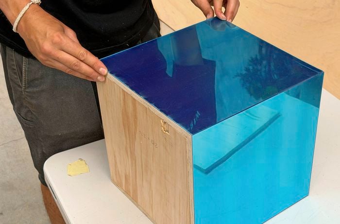 Hands applying acrylic mirrors to the side of a wooden box.