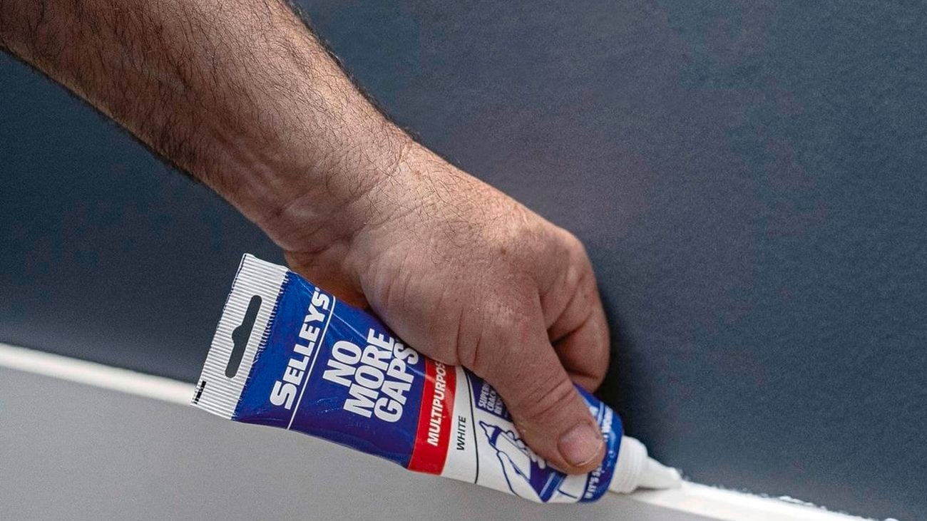 A hand uses Selleys No More Gaps on a white skirting board.
