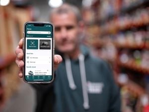 A close-up of a man’s hand holding a phone that shows the Bunnings Trade PowerPass app in use