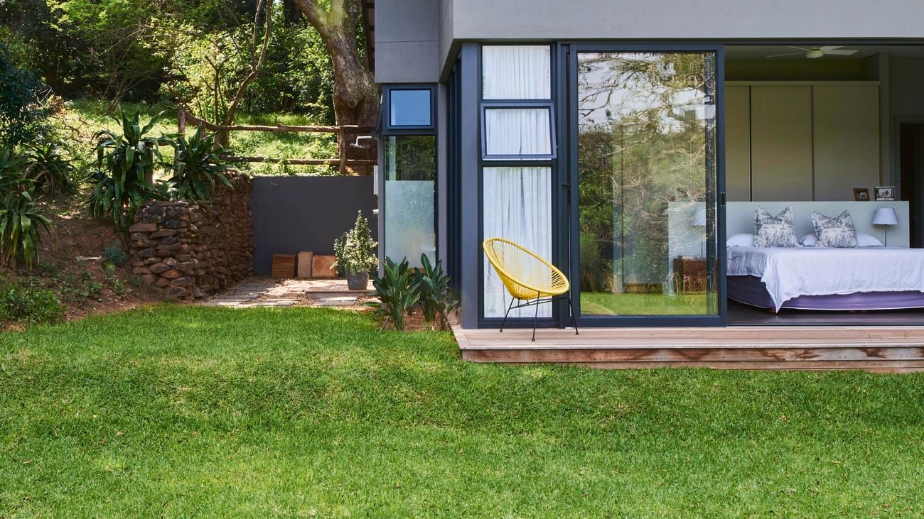 A house with a bed in a bedroom, with glass doors opened onto a backyard