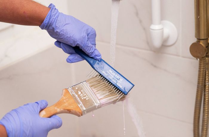 Person cleaning a paint brush with a brush comb