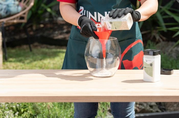 Person funnelling sand into see-through glass pot.