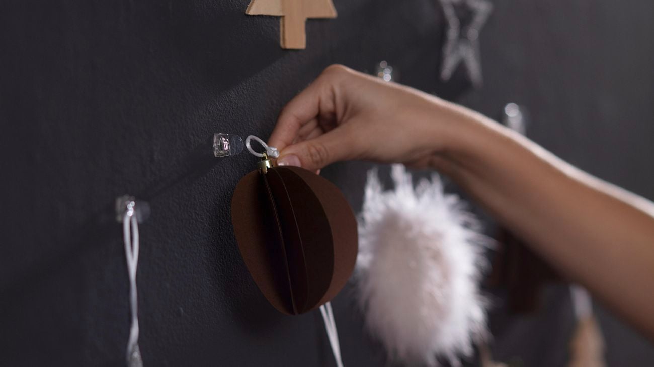 Hand hanging up Christmas decorations on clear hooks attached to a dark wall