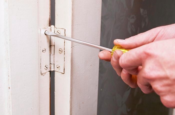 Person unscrewing screw in door hinge.