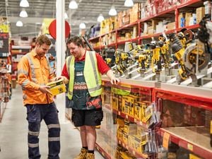 Team member and customer discussing power tools in a Bunnings store aisle, with various drills and toolboxes displayed on shelves.