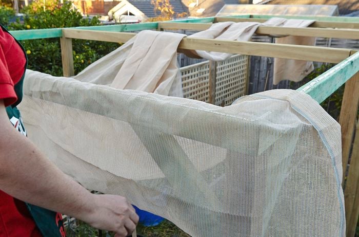A shade cloth being stretched out over a wooden frame by a Bunnings team member on a ladder