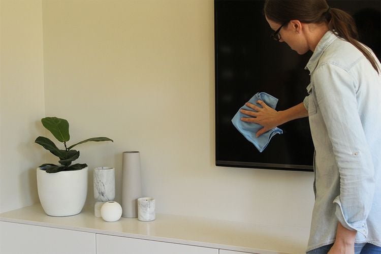 Person cleaning a TV screen with a microfibre cloth