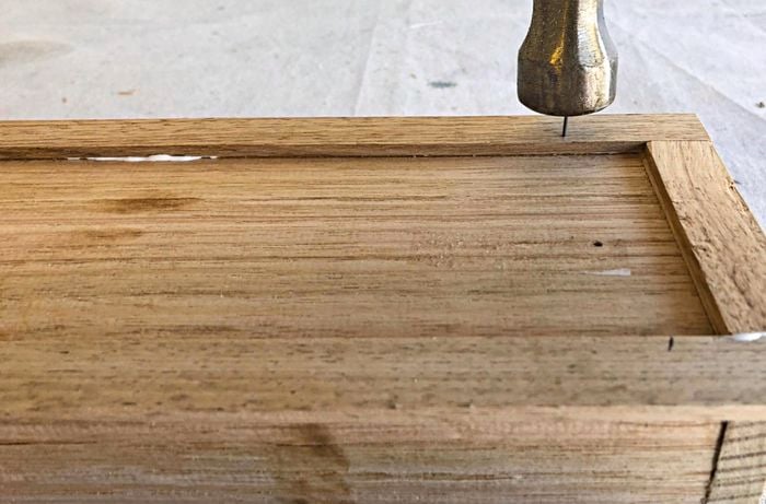 Person hitting nail into piece of edging so that it joins with planter base.