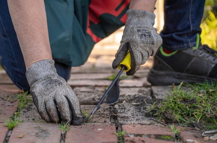 Bunnings team member wearing gloves using a weed tool to remove weeds on pathway.