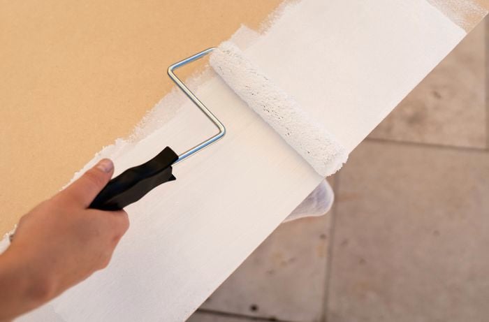   A person is applying primer to an MDF panel with a paint roller to prepare the surface for chalkboard paint.