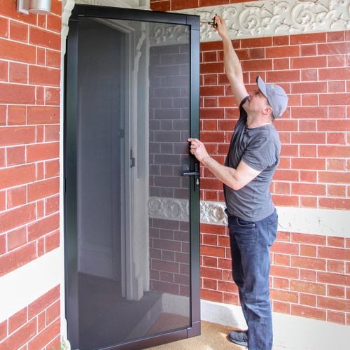 A man installing a security door at the front of the house