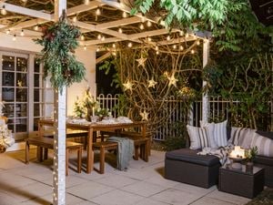 Outdoor patio decorated with string lights, wooden dining table, and cushioned seating under a pergola.