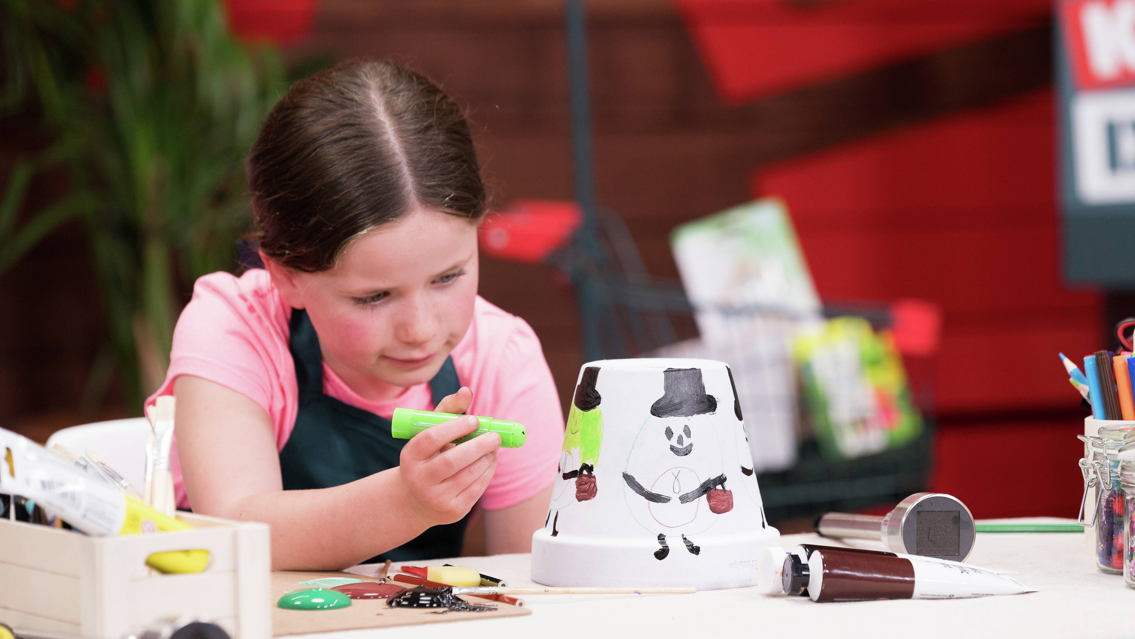 A young girl is applying green colour to the face on a pot