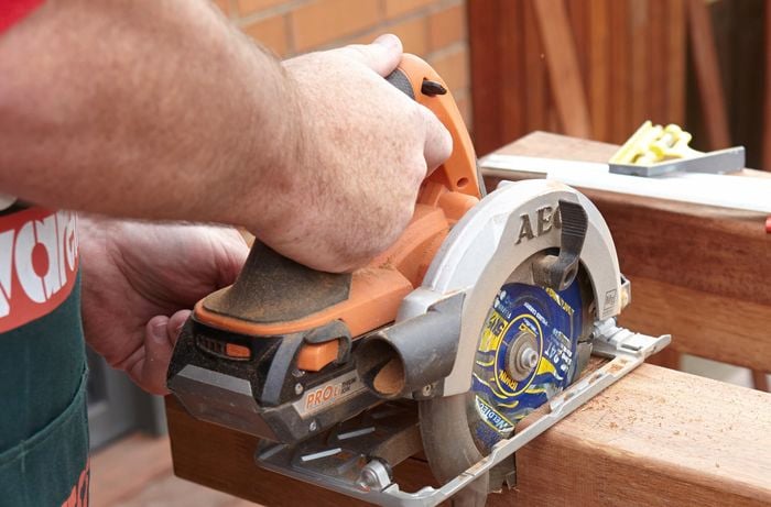 Person using circular saw to cut through pergola frame piece.