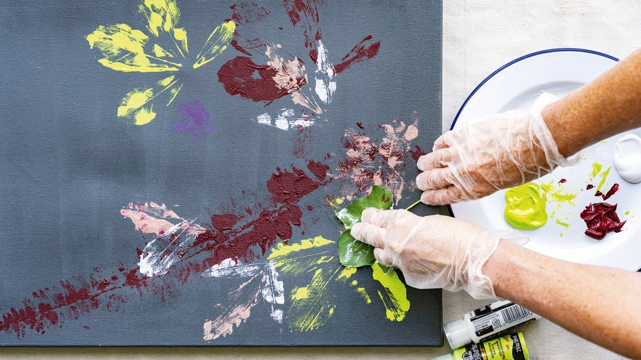 Two gloved hands hold down a leaf on a grey/blue canvas to create a D.I.Y. botanical artwork