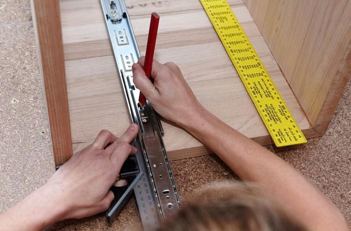 A person marking hole positions for a metal drawer runner