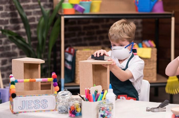 A boy with a mask on sanding a wooden tool caddy.