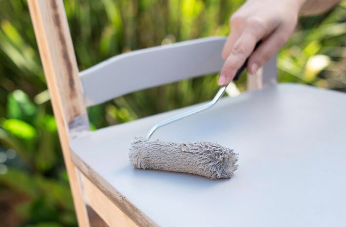 Person painting chair with roller.