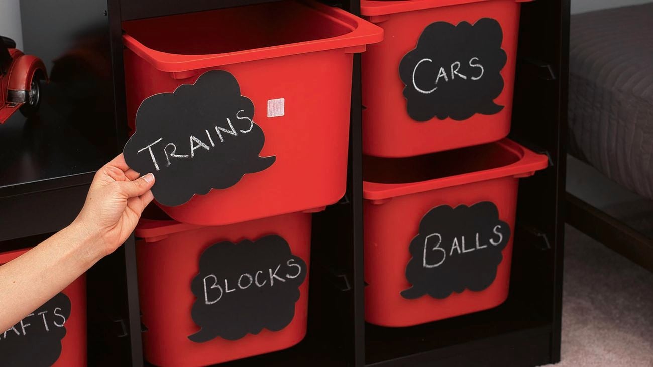 VELCRO® sticks signs reading, ‘trains,’ ‘cars,’ ‘blocks,’ and ‘balls,’ on red containers