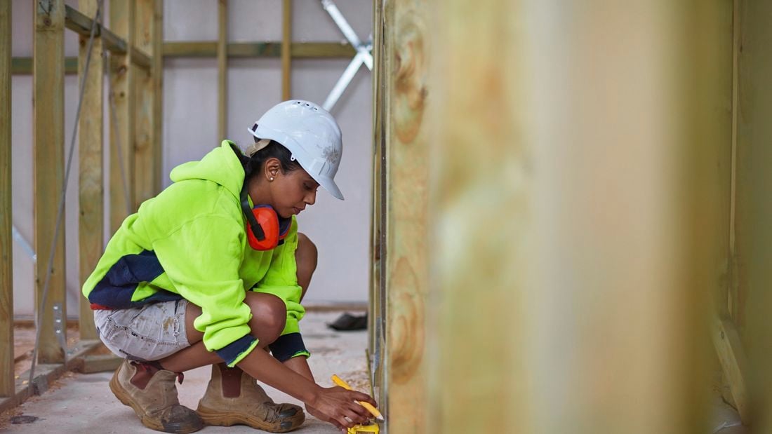 A construction worker measuring the base of a wooden frame with a tape measure on a building site
