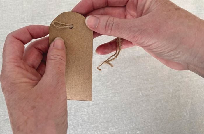 Hands thread twine through hole in cardboard