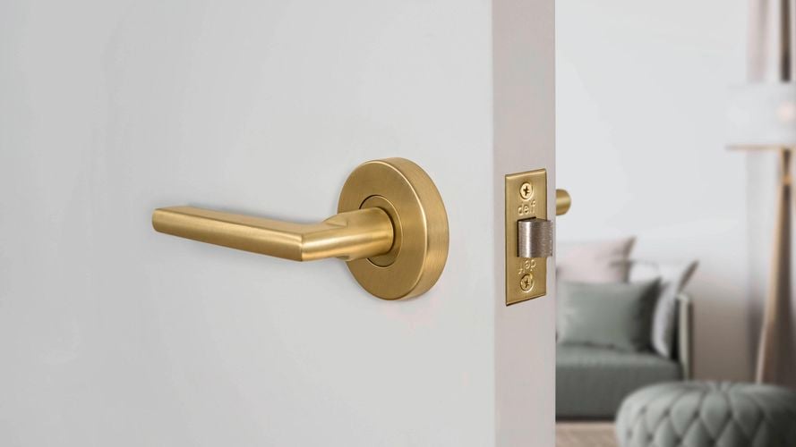 A Delf Madrid Lever Set Satin Brass door handle on a white door to a living area