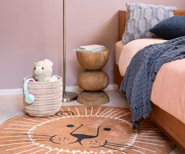 A kids bedroom with a bed, rug, cane basket and light stand in it.