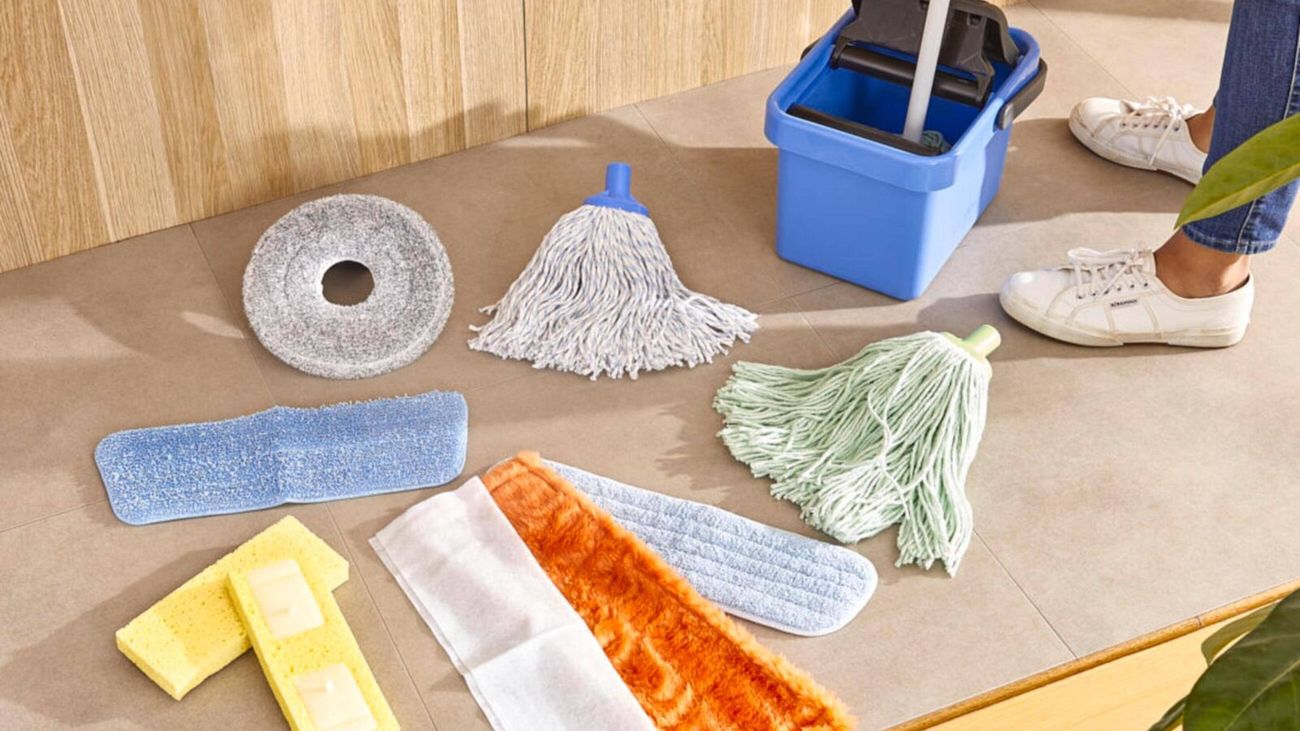 A mop is dipped into a blue bucket, with an array of different mop-head attachments laid out nearby