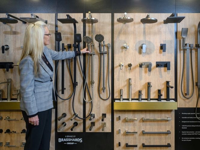 A lady standing in front of a wall with a variety of shower heads and tapware on it.