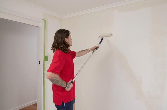 An individual in a red T-shirt is rolling up a paint roller on the wall.