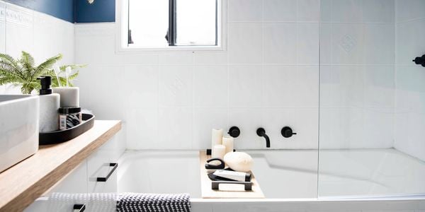 A white tiled bathroom, with black tapware over a white bath and a deep blue feature wall showcasing a bathroom design idea.