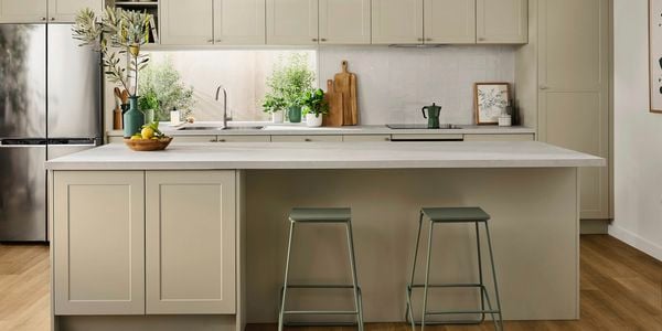 A modern New Rural kitchen featuring soft sage green shaker cabinets, light stone benchtops, timber flooring, and potted greenery for a fresh, natural look