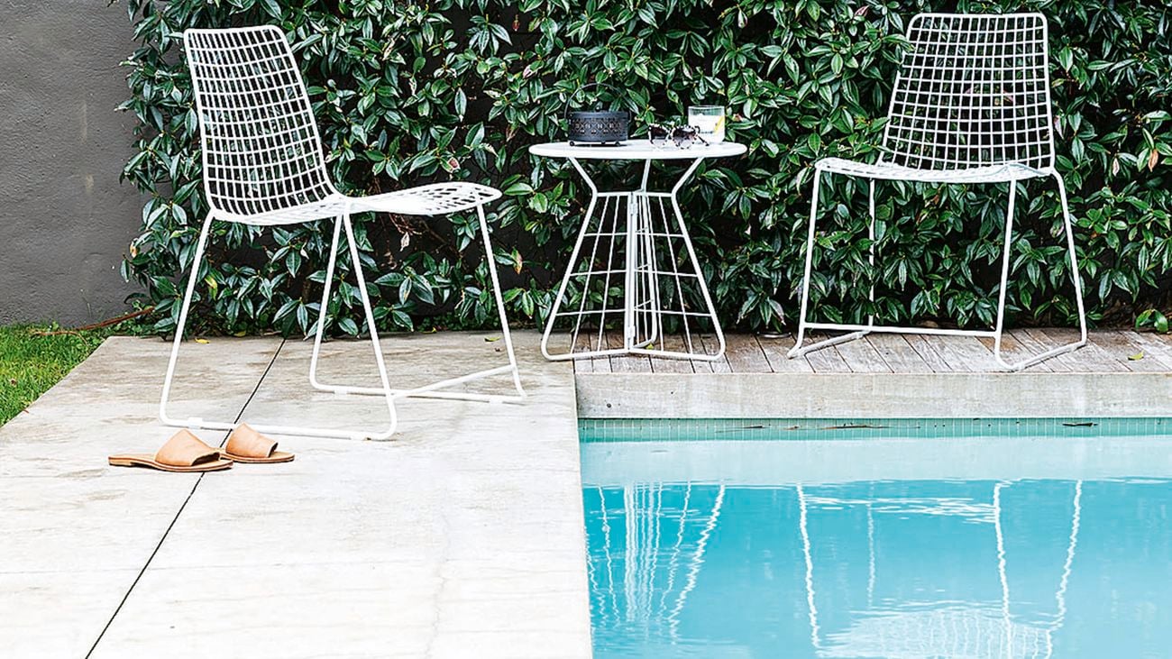 A pool with outdoor tiles and some chairs.