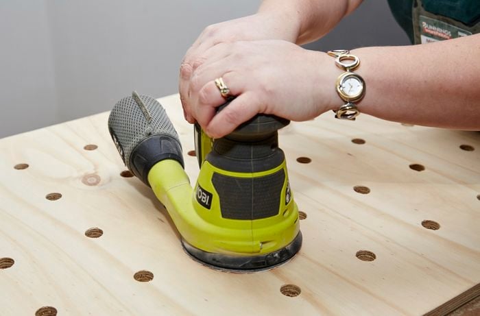 A person sanding a sheet of plywood using an orbital sander