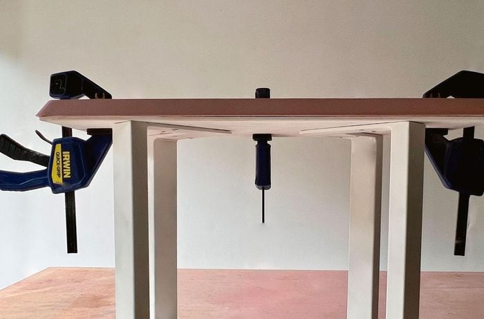 Clamps holding a pink terrazzo tabletop, table base and legs together.