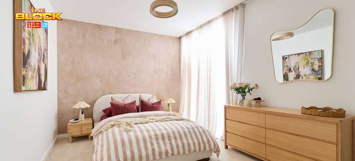 Contemporary bedroom featuring striped neutral bedding, a curved bedhead, timber dresser, statement mirror and soft pink feature wall.