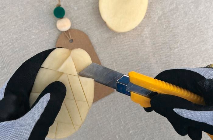 Hands wearing safety gloves use utility knife to cut Christmas tree into potato